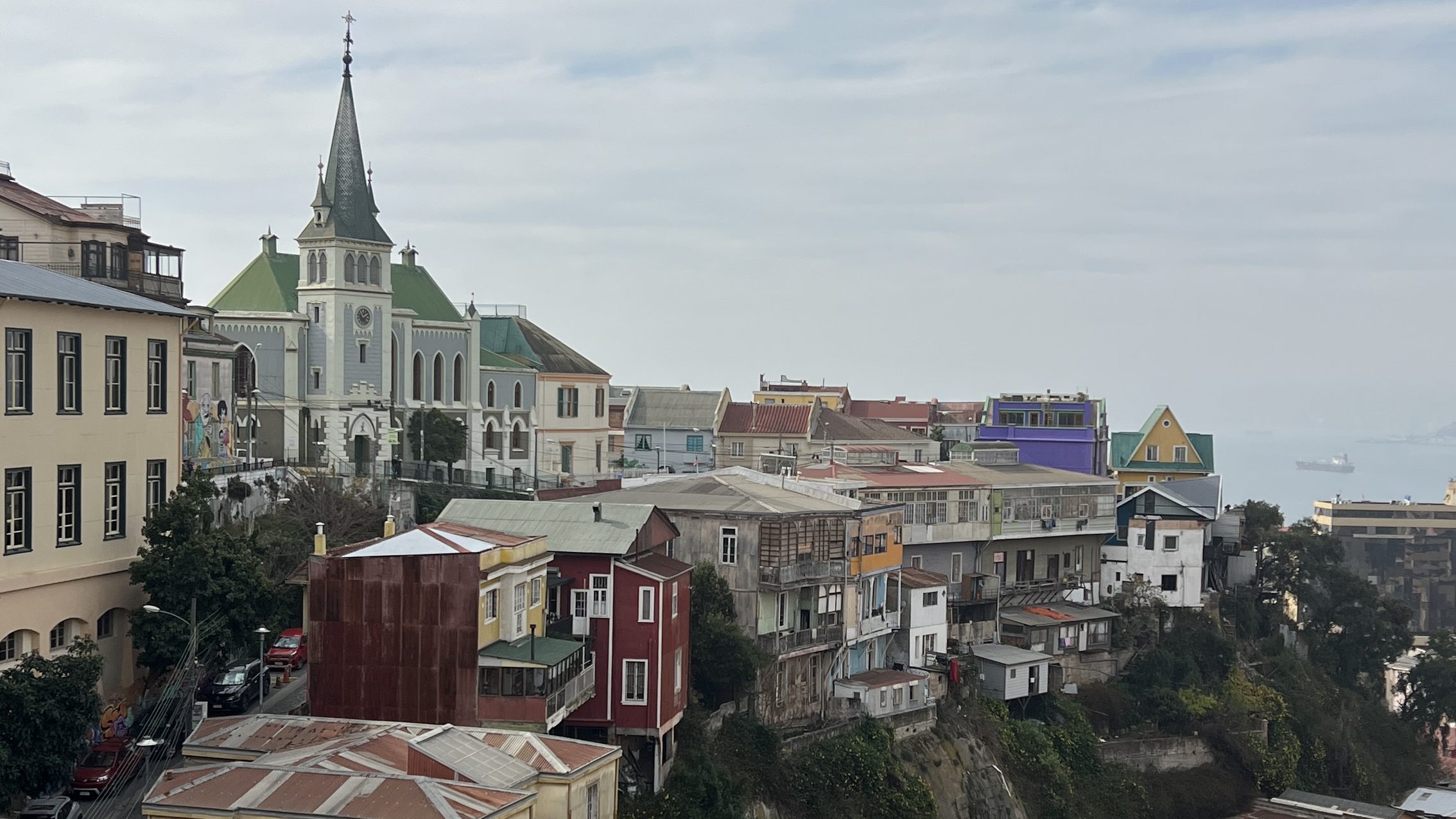 Colorful hillside buildings, street murals, and a church spire overlooking the sea in Valparaíso.